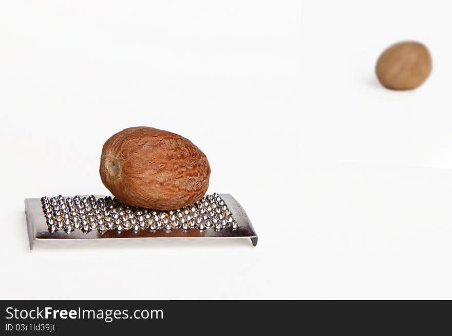 One nutmeg on a grater, with other in the upper right corner, isolated on white background. One nutmeg on a grater, with other in the upper right corner, isolated on white background.