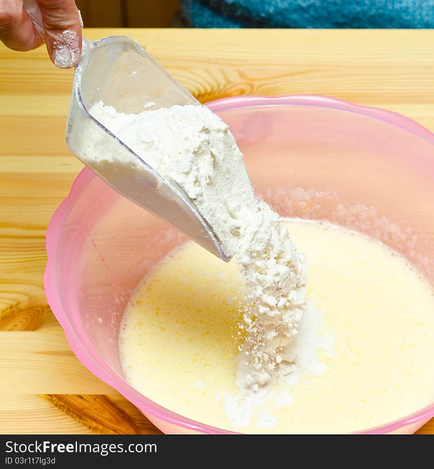 Making cookies. Pouring flour into a pink bowl on wooden table.