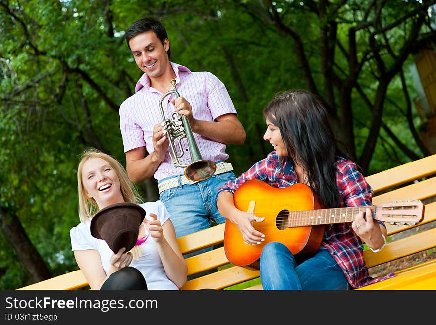 Young friends play the guitar and trumpet in the park