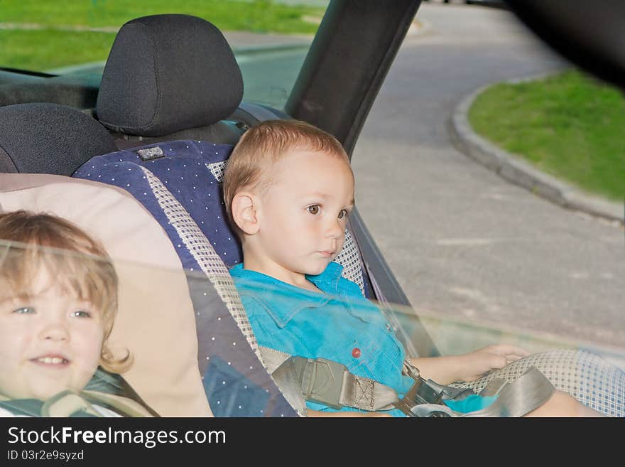 Two little kids sitting on back seat in child safety seats looking on windows. Two little kids sitting on back seat in child safety seats looking on windows