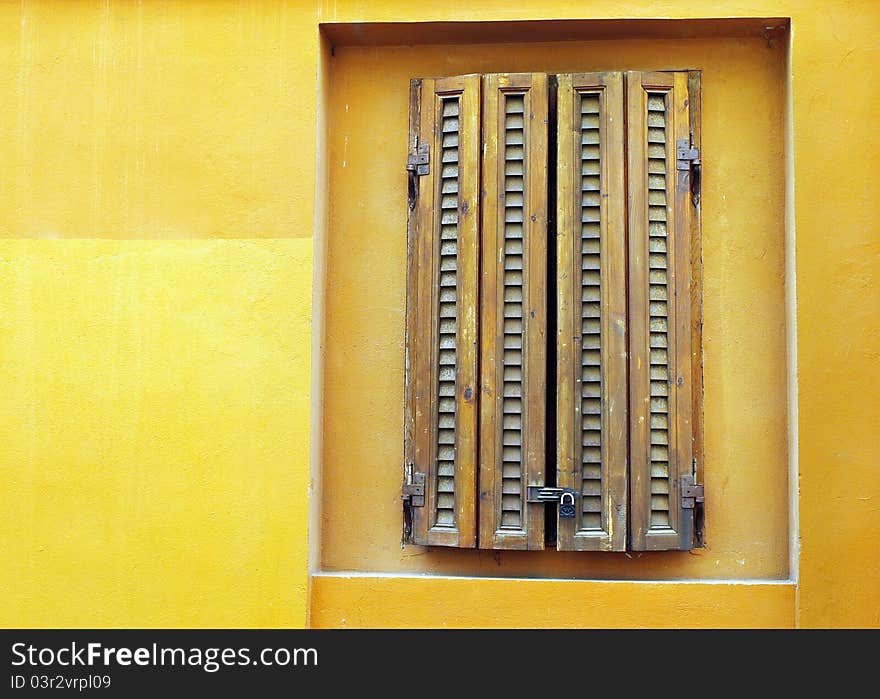 A background with a view of a closed window on an old yellow wall.