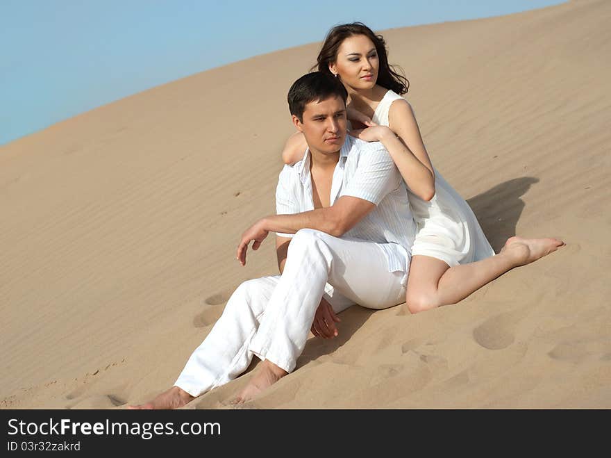 Young couple in love in a white dress sitting on sand. Young couple in love in a white dress sitting on sand