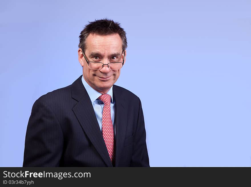 Smiling Business Man in Suit with Cheesy Expression Looking Over Glasses on Blue Background. Smiling Business Man in Suit with Cheesy Expression Looking Over Glasses on Blue Background