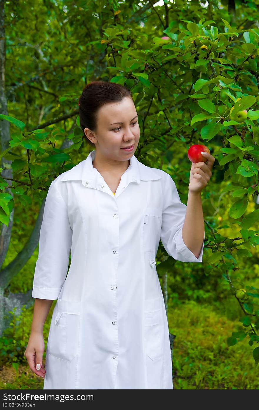 A pretty woman doctor handing an apple in the apple garden. A pretty woman doctor handing an apple in the apple garden