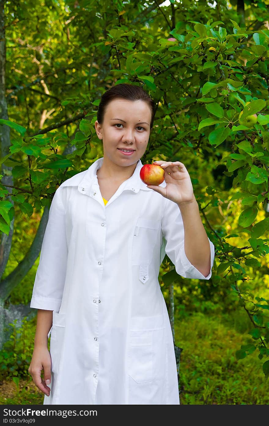 A pretty woman doctor handing an apple in the apple garden. A pretty woman doctor handing an apple in the apple garden