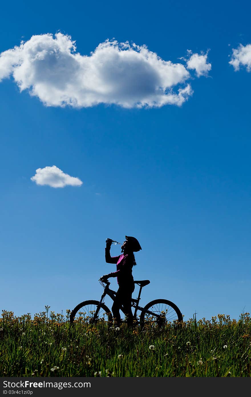 Silhouette of female mountain biker drinking from water bottle in a meadow. Silhouette of female mountain biker drinking from water bottle in a meadow.