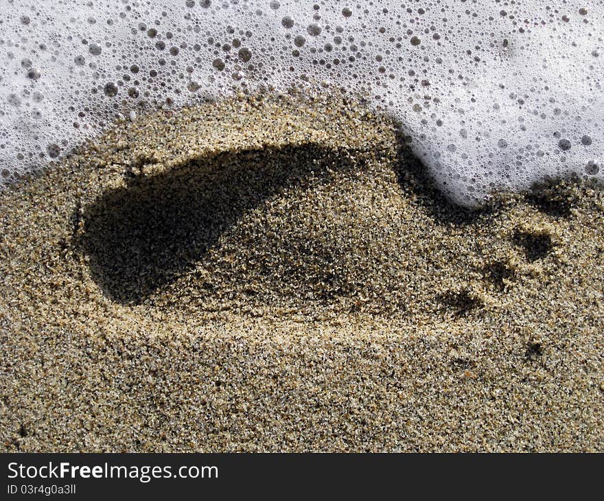 Sea foam washing away foot print in the sand. Sea foam washing away foot print in the sand