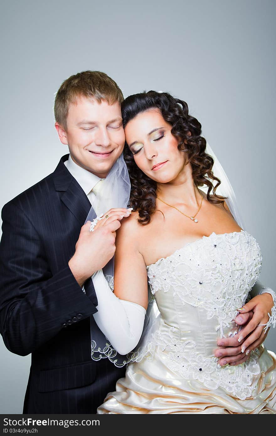 Studio portrait of young beautiful happy just married bride and groom with closed eyes embracing on blue background