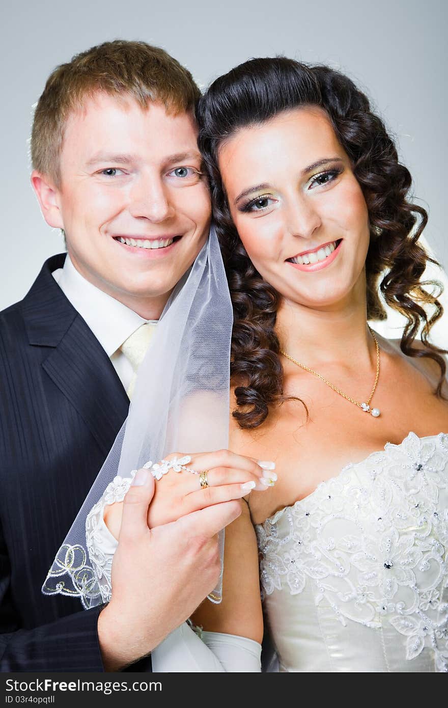 Studio portrait of young elegant enamored just married bride and groom and embracing on grey background