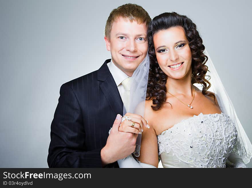 Studio portrait of young elegant enamored just married bride and groom and embracing on grey background