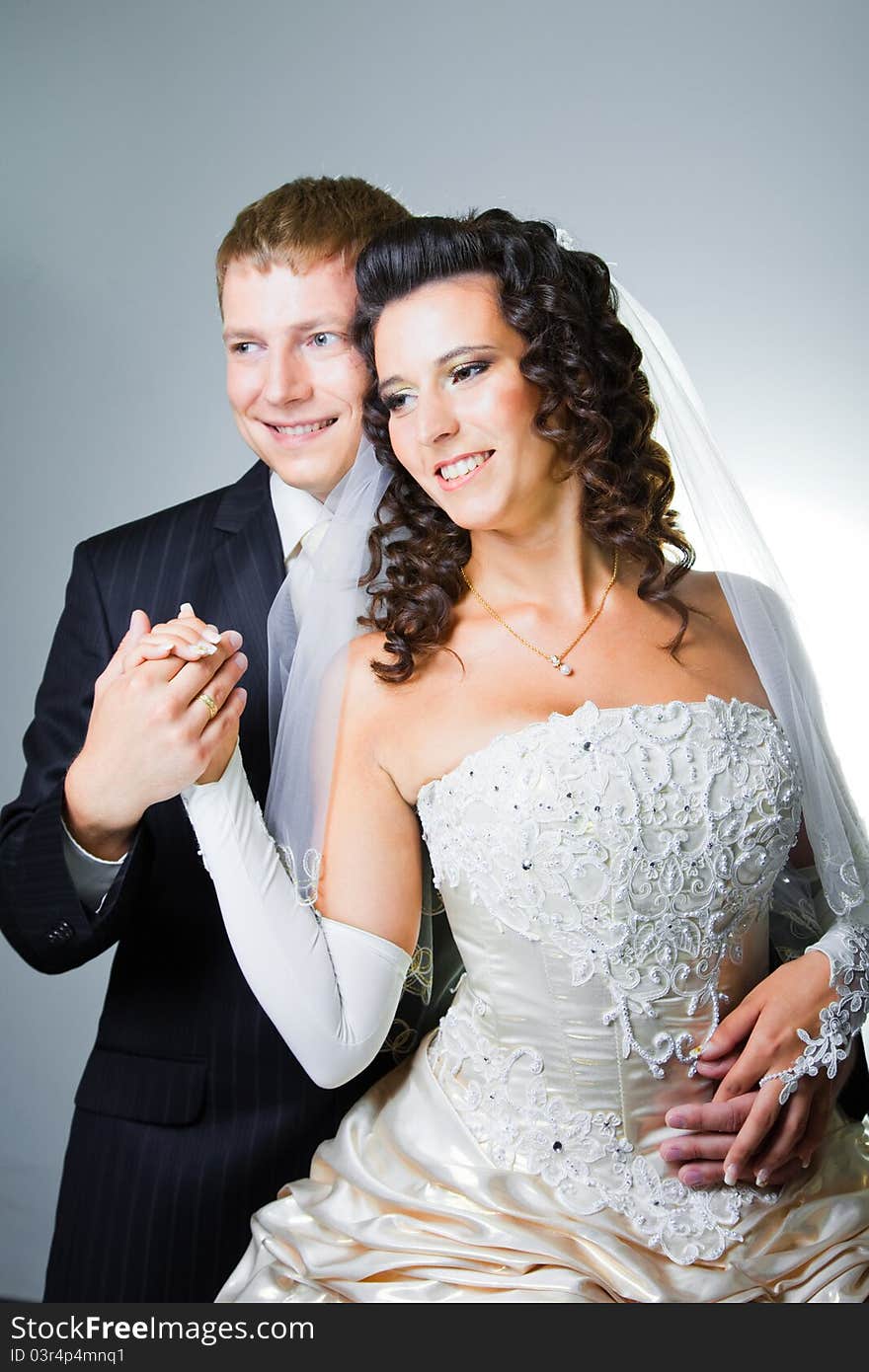 Studio portrait of young elegant enamored just married bride and groom and embracing on grey background