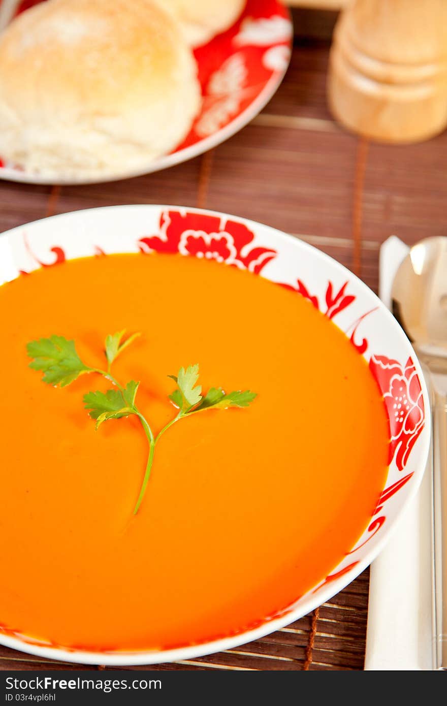 A bowl of tomato soup with bread in the background.