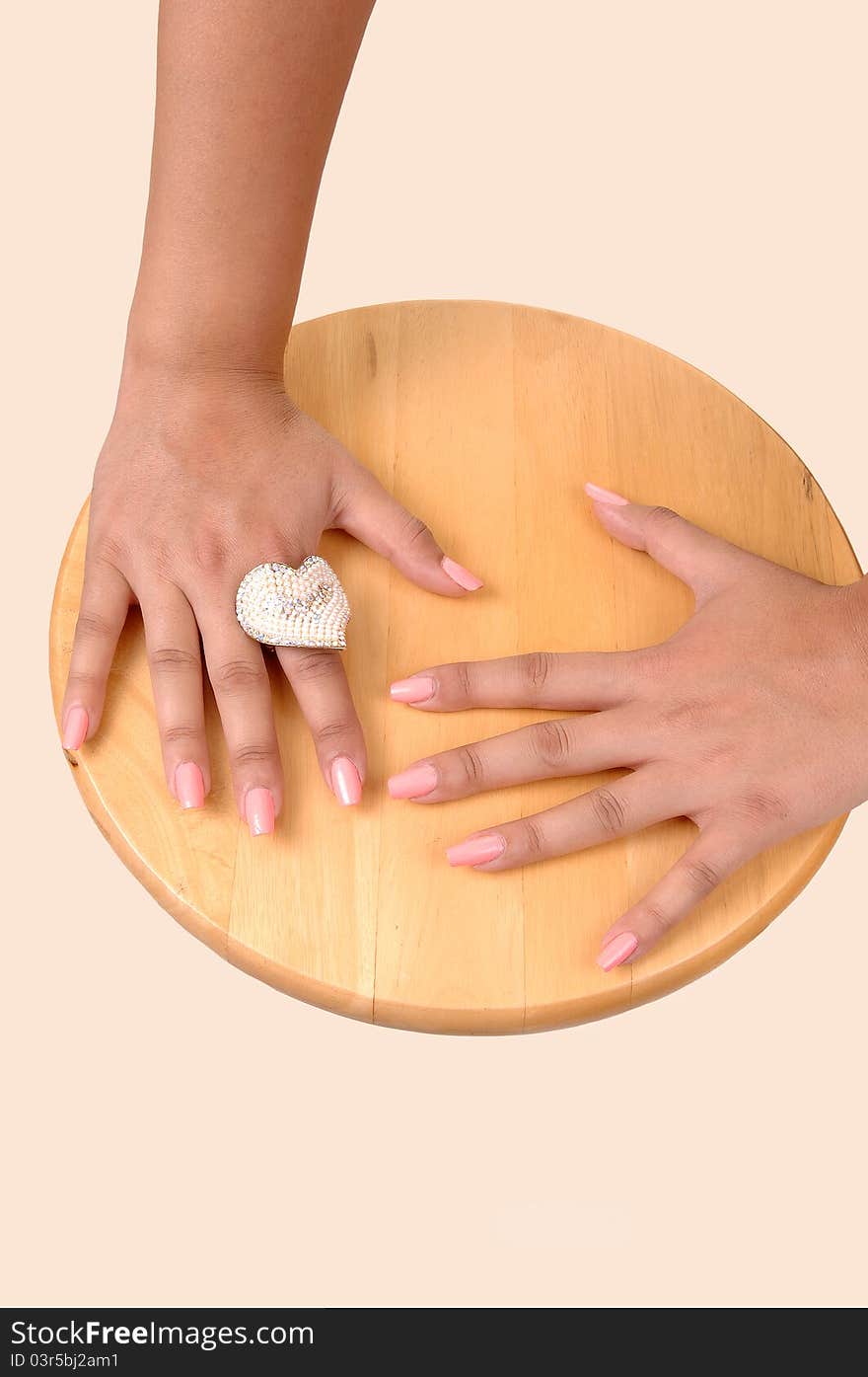 The hands of a teenager resting of a wooden plate with a big silver ring on one finger and polished finger nails, for beige background. The hands of a teenager resting of a wooden plate with a big silver ring on one finger and polished finger nails, for beige background.