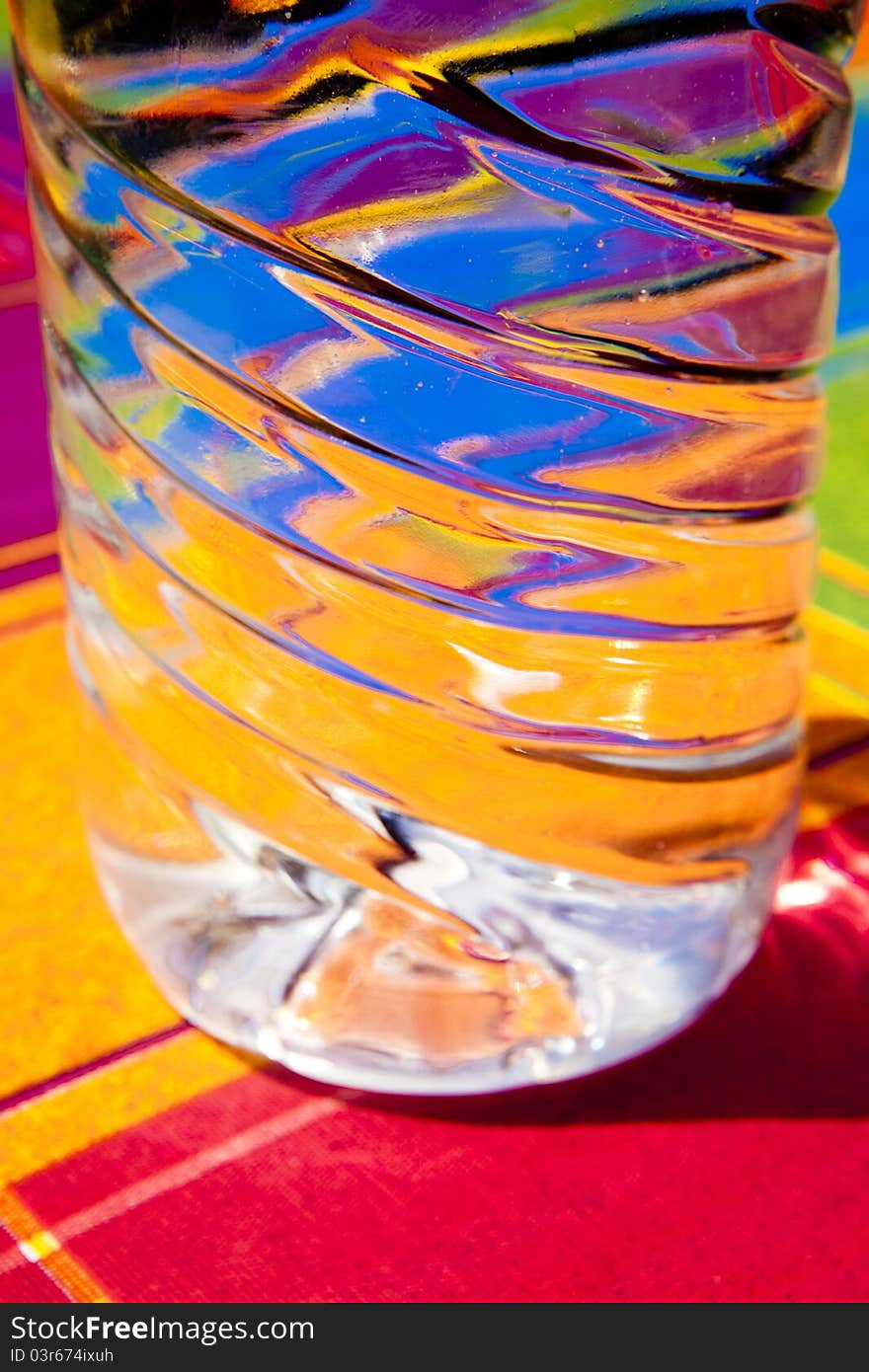 Water reflection of colors within a transparent plastic bottle on a table with tablecloth colors. Water reflection of colors within a transparent plastic bottle on a table with tablecloth colors