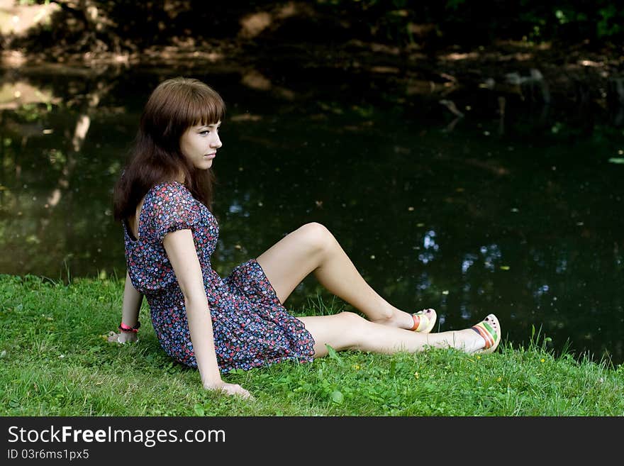 Beautiful girl sitting on bank of a river in summer