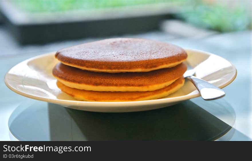 Stack of 3 pancakes on a plate with a garden in the background. Stack of 3 pancakes on a plate with a garden in the background