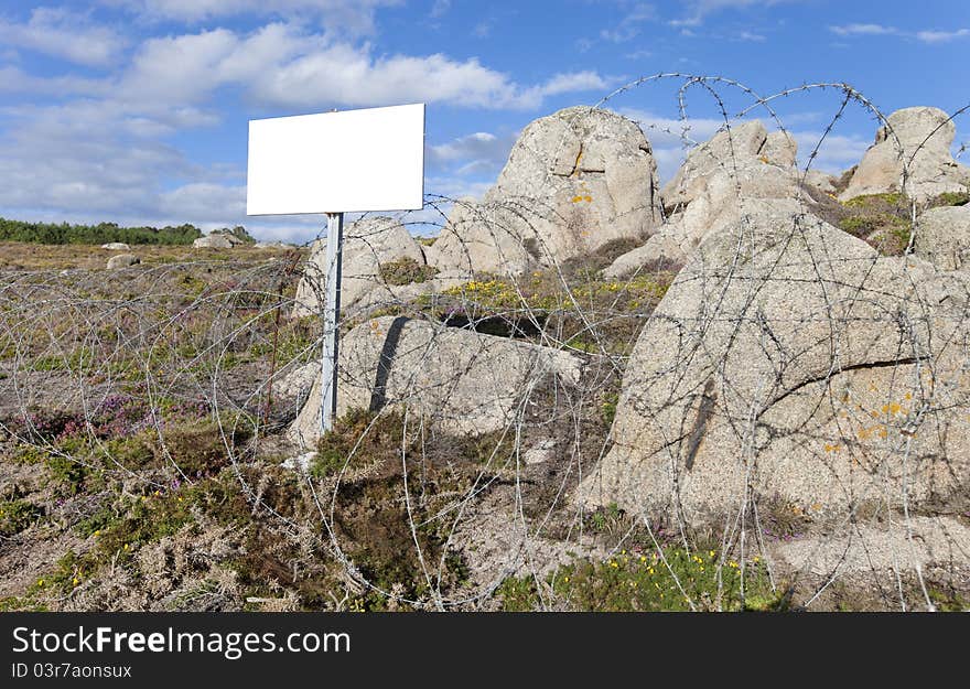 Barrier to nature with barbed wire, white sign, blue sky