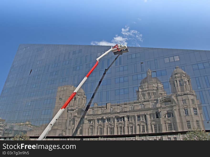 A Red and White Cherry Picker and Glass Building with Reflection of a Historic Building