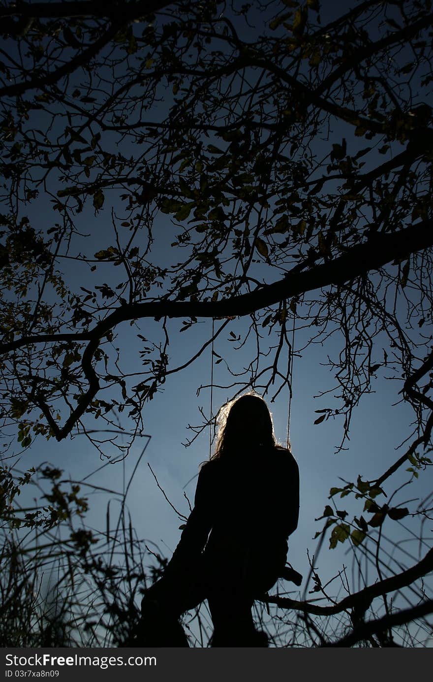 A sillhouette of person sitting on a swing. A sillhouette of person sitting on a swing