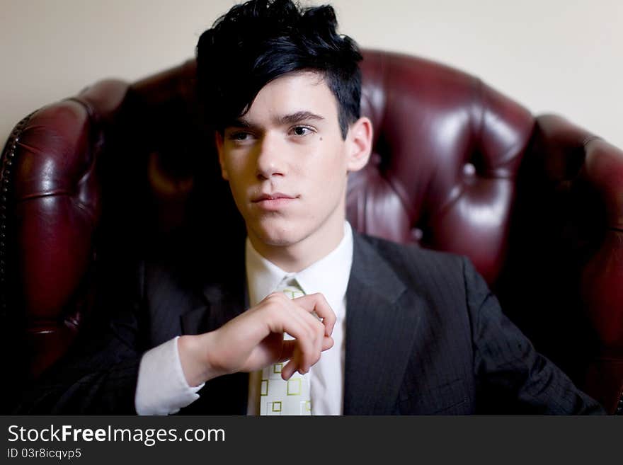 A handsome young man in a business suit, seated on a plush leather chair, looking camera left. A handsome young man in a business suit, seated on a plush leather chair, looking camera left.