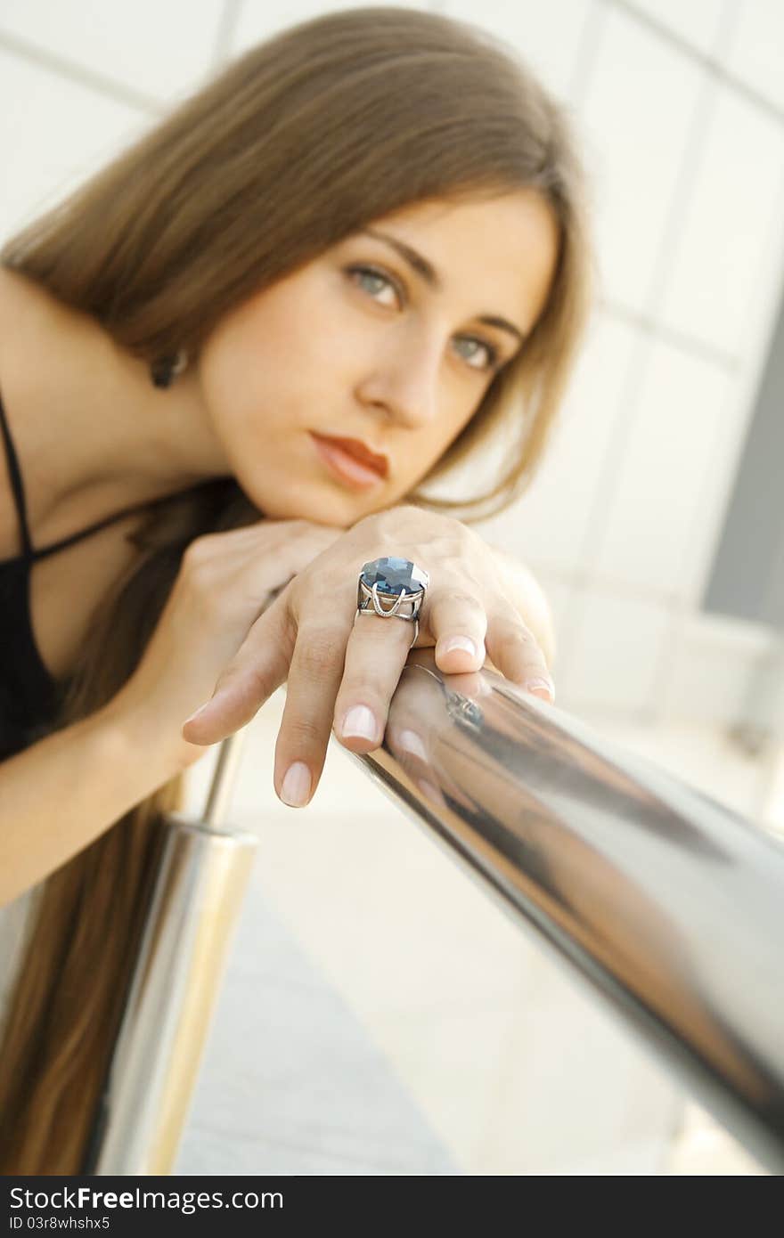 Portrait of elegantly beautiful young woman is based on the railing. The girl beautiful jewelry, ring and earrings with large blue stones