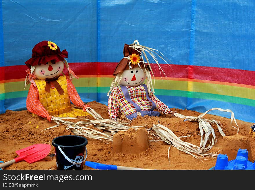 Two colourful scarecrows sitting on the sand with a wind break and buckets and spades. Two colourful scarecrows sitting on the sand with a wind break and buckets and spades