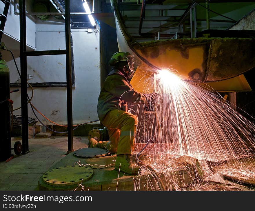 A workman flame cutting a lage metal tank. A workman flame cutting a lage metal tank