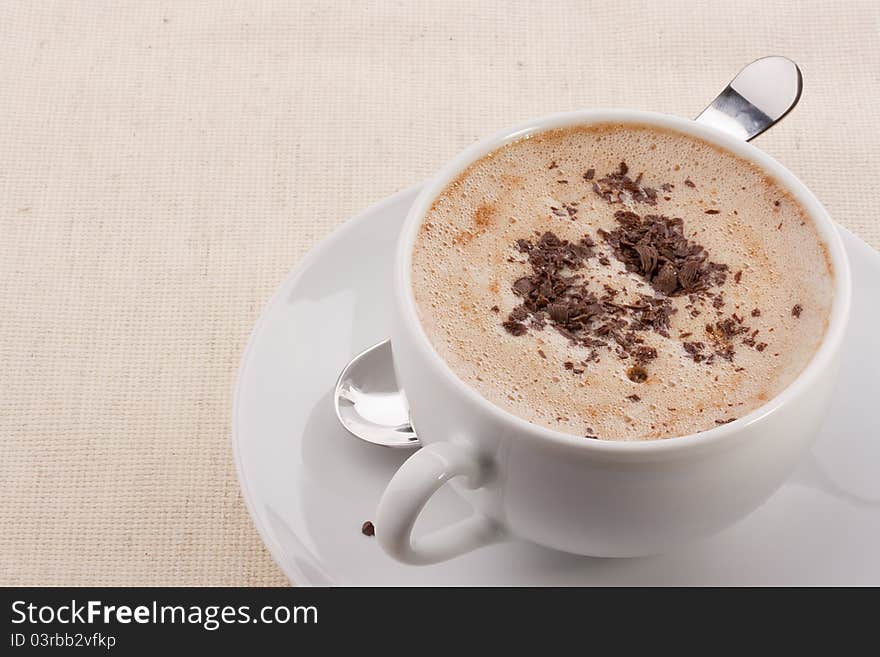 Cappuccino in a white ceramic cup with a saucer and a spoon.