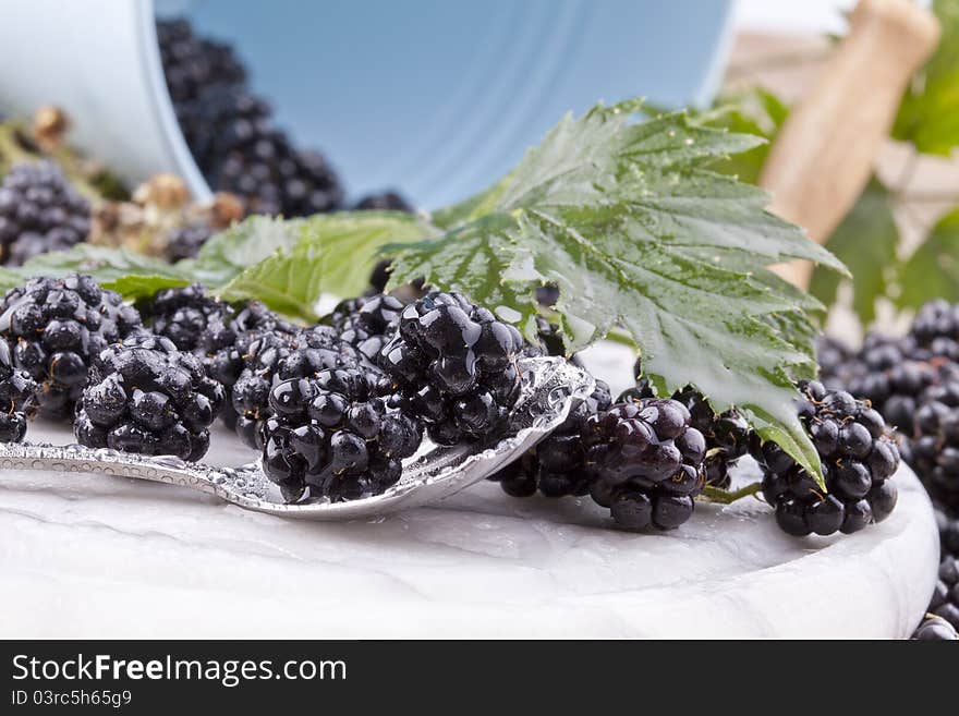 Studio- shot of blackberries with waterdrops on a spoon and a bucket in the background.