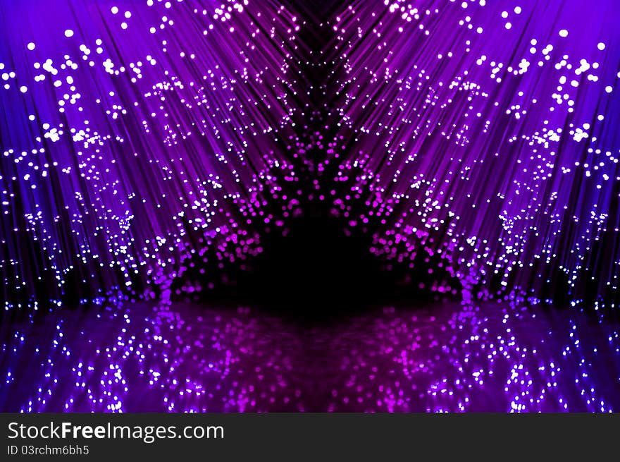 Close up on two groups of illuminated blue and magenta fiber optic light strands against a black background and reflecting into the foreground. Close up on two groups of illuminated blue and magenta fiber optic light strands against a black background and reflecting into the foreground.