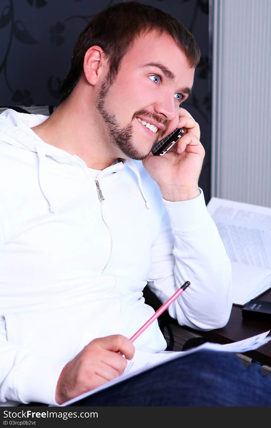 Young and attractive guy calling by phone and write something in notebook. Young and attractive guy calling by phone and write something in notebook