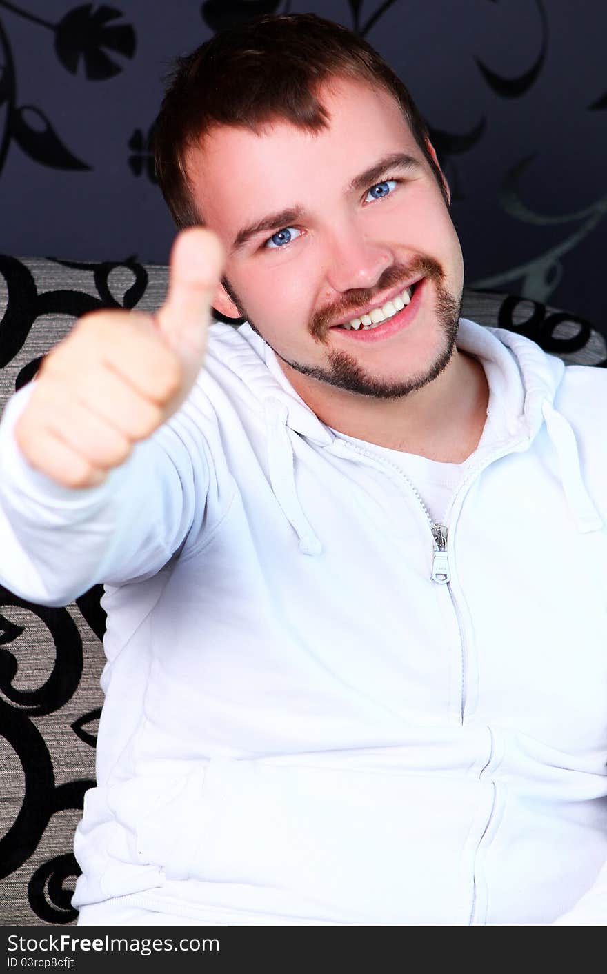 Young guy sitting on sofa and shows OK sign. Young guy sitting on sofa and shows OK sign