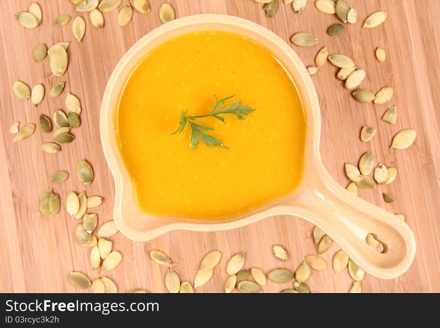 Pumpkin soup decorated with parsley and pumpkin seeds on wooden background