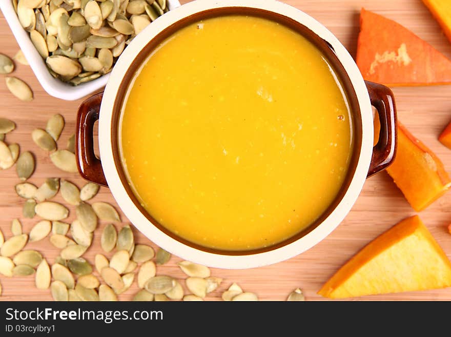 Pumpkin soup, a bowl of pumpkin seeds and some pieces of pumpkin on wooden background