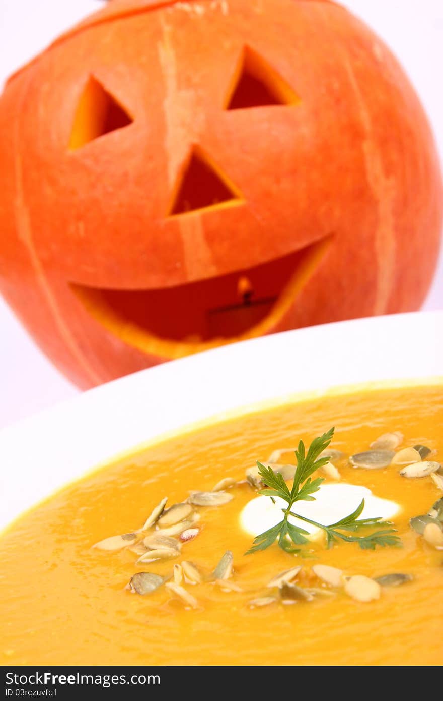 Pumpkin soup decorated with cream, pumpkin seeds and parsley with Jack-o'-lantern in the background