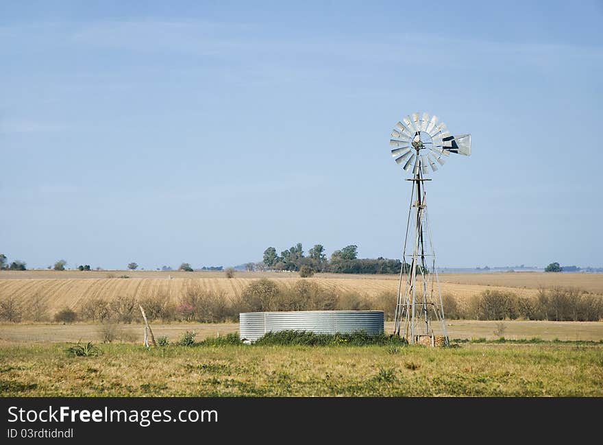 A windmill for pumping water and a metallic tank in the country. Province of Entre Rios, Argentina. A windmill for pumping water and a metallic tank in the country. Province of Entre Rios, Argentina.