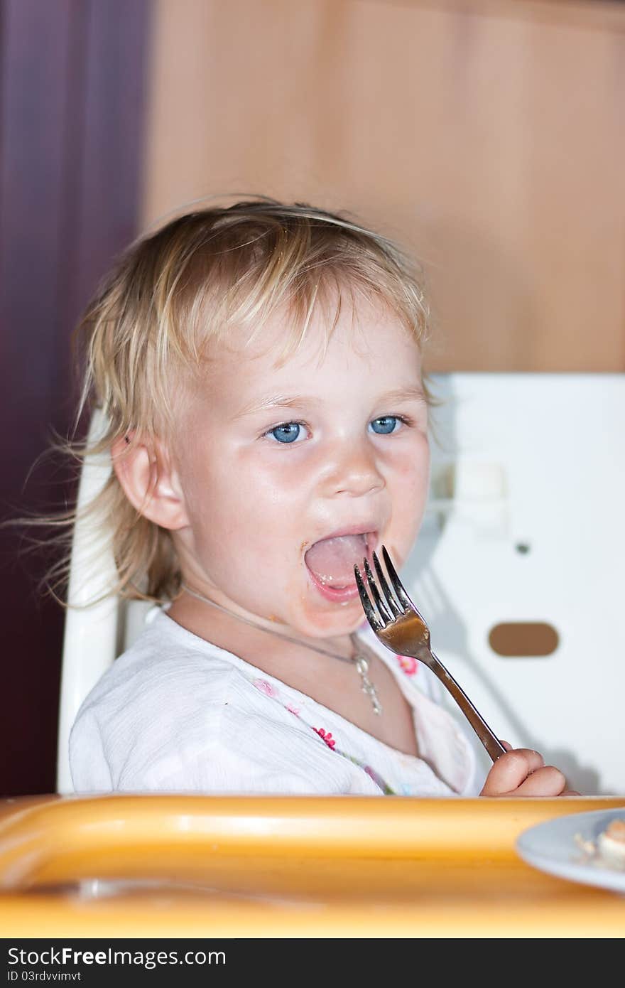 Adorable baby eating cake in a chair with a fork