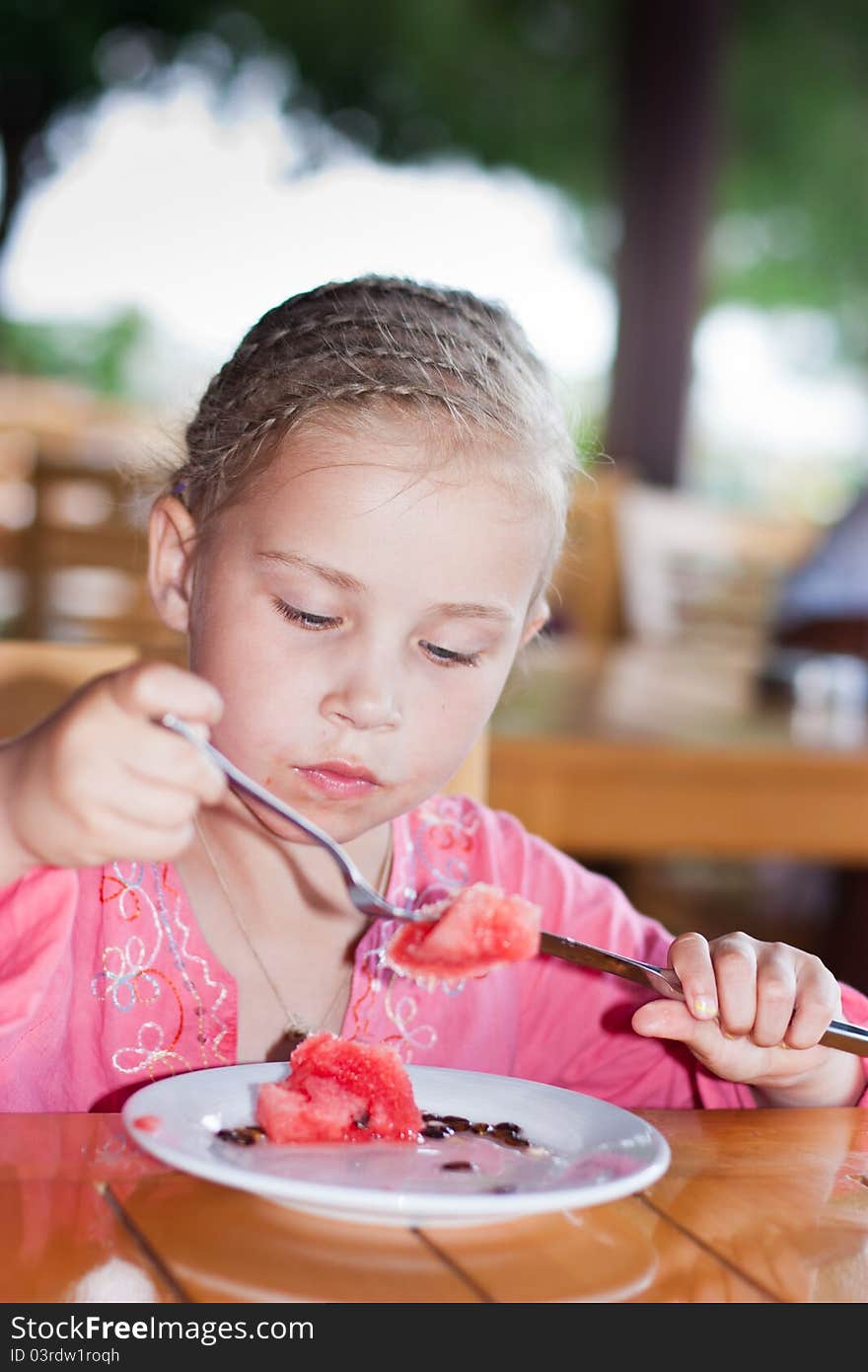 Adorable girl eating watermelon with a knife and a fork outdoor. Adorable girl eating watermelon with a knife and a fork outdoor