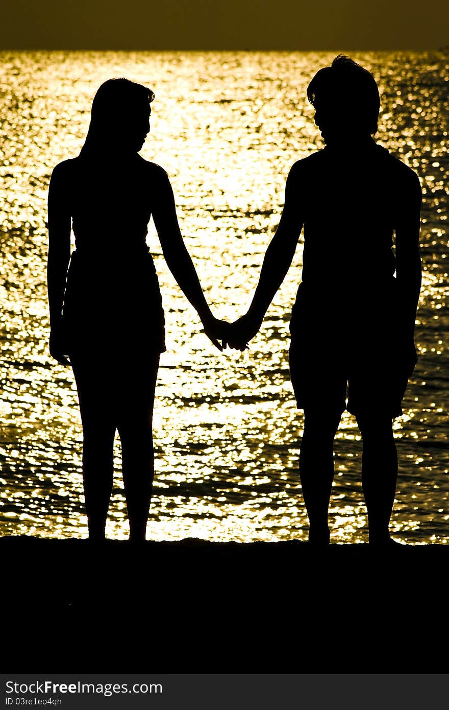 The shot of Couple standing on the beach, holding hand and look to each other. The shot of Couple standing on the beach, holding hand and look to each other.