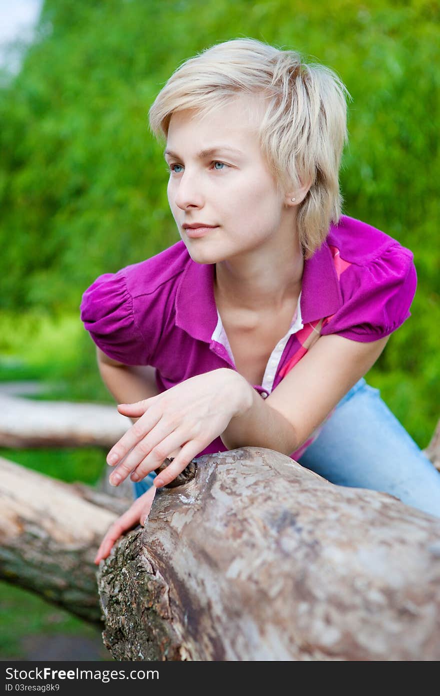 Beautiful young blonde woman outdoors in the park sitting on the tree branch. Beautiful young blonde woman outdoors in the park sitting on the tree branch