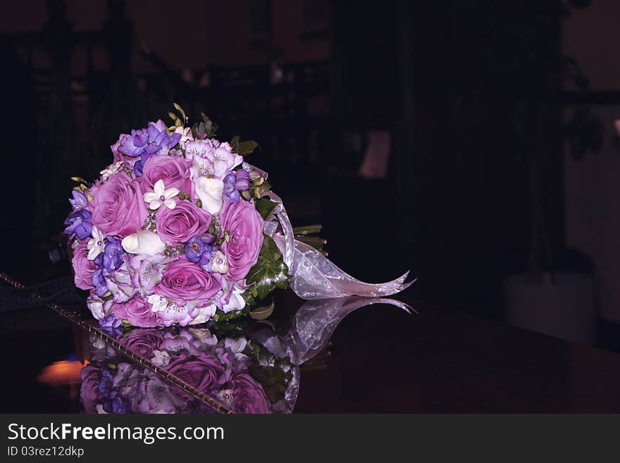 A bride's bouquet of purple, pink and white flowers tied with ribbon set down on a shiny black piano. A bride's bouquet of purple, pink and white flowers tied with ribbon set down on a shiny black piano.