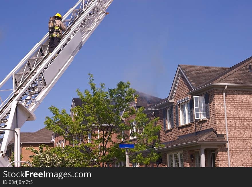 Firefighter wearing a self contained breathing apparatus on an engine ladder surveys an extinguished fire that damaged a roof top. Firefighter wearing a self contained breathing apparatus on an engine ladder surveys an extinguished fire that damaged a roof top.