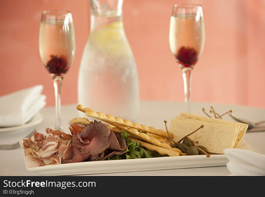 Entree dish with pastry crackers,roast beef,prosciutto,salami and rocket with 2 glasses and a bottle of water on the background. Entree dish with pastry crackers,roast beef,prosciutto,salami and rocket with 2 glasses and a bottle of water on the background