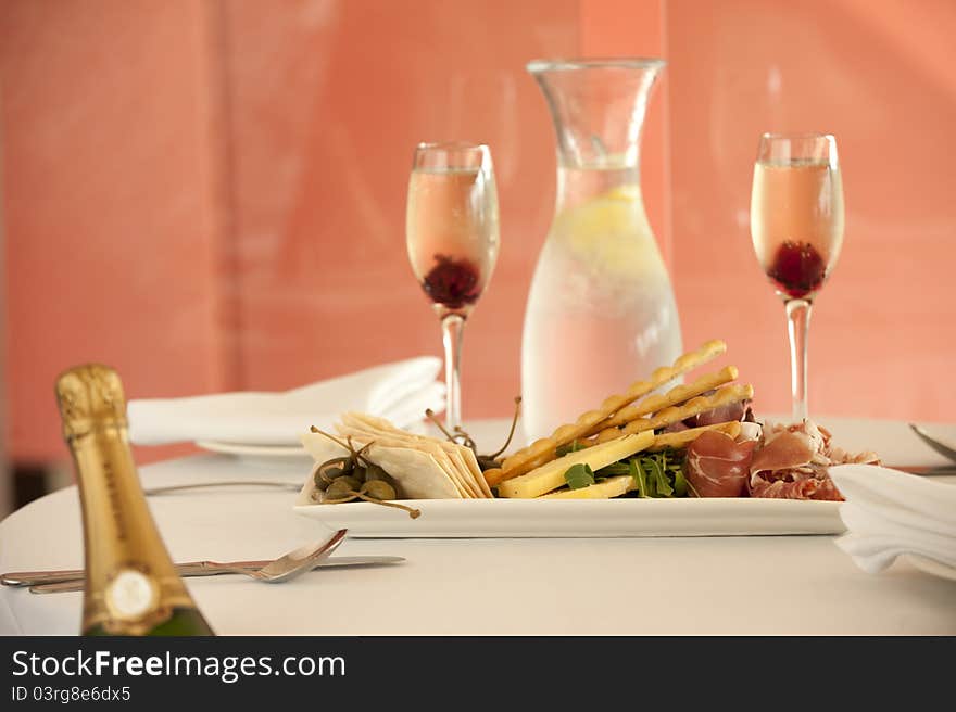 Entree dish with pastry crackers,roast beef,prosciutto,salami and rocket with 2 glasses and a bottle of water on the background. Entree dish with pastry crackers,roast beef,prosciutto,salami and rocket with 2 glasses and a bottle of water on the background