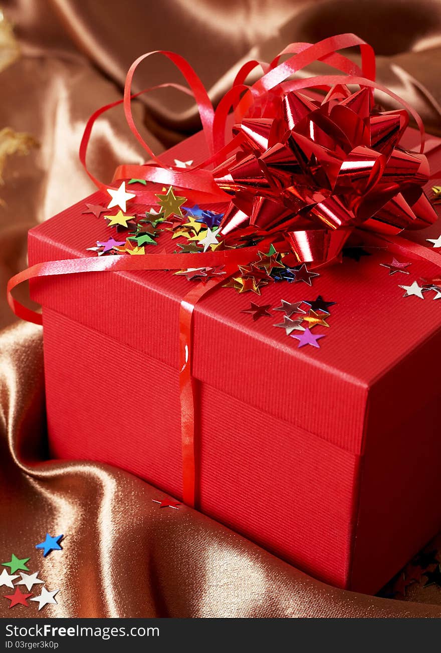 Red gift box with bows and stars on golden silk background