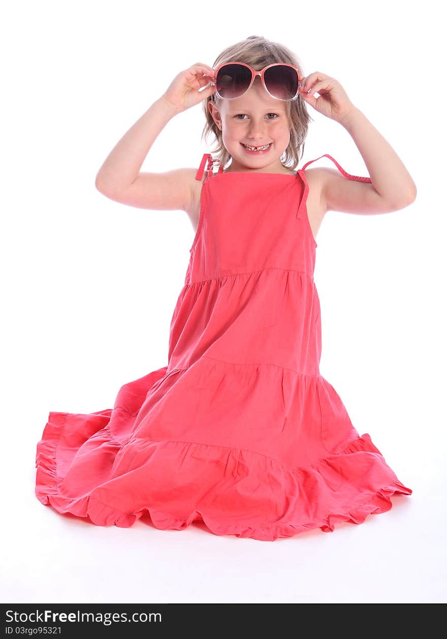 Cute blonde six year old primary school girl wearing coral pink dress kneeling on the floor having fun with sunglasses. Cute blonde six year old primary school girl wearing coral pink dress kneeling on the floor having fun with sunglasses.