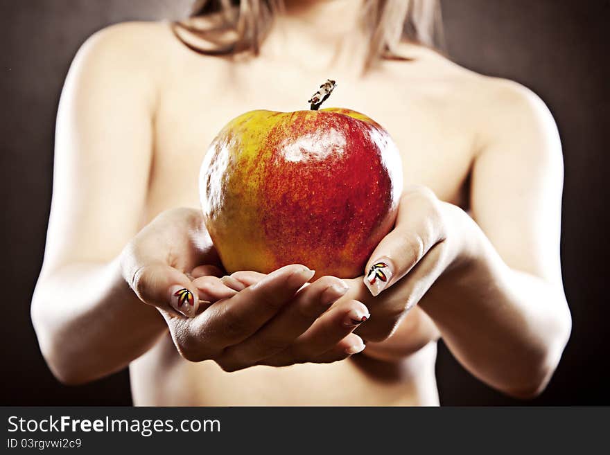 Beautiful topless woman is holding a red and yellow beautiful apple in front of her breasts. The focus is on the apple. Beautiful topless woman is holding a red and yellow beautiful apple in front of her breasts. The focus is on the apple.