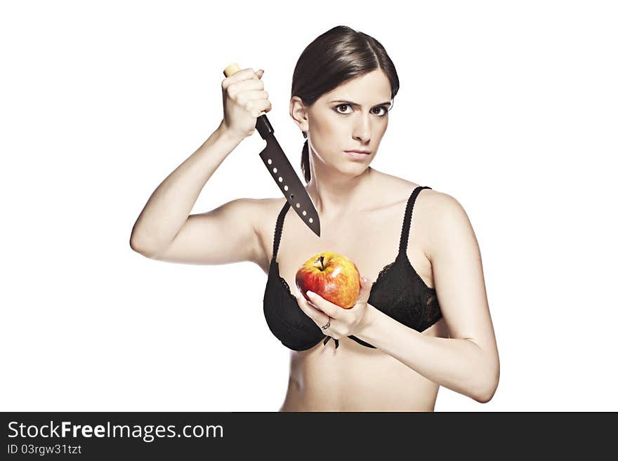 Dangerous looking woman, in a black lace bra is trying to stab a beautiful apple, on a white background. Dangerous looking woman, in a black lace bra is trying to stab a beautiful apple, on a white background.