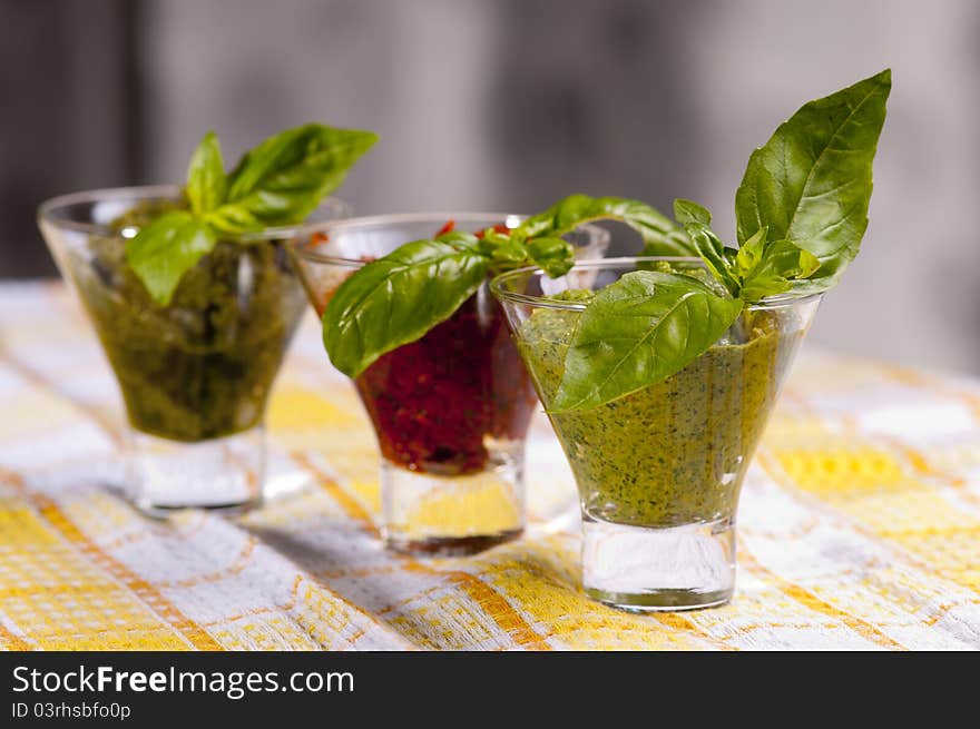 Three kind of pestos in small glasses with few leaves of basil