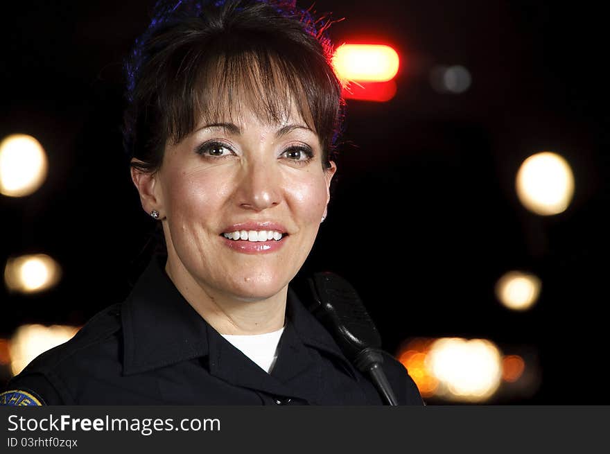 A Hispanic female police officer standing in the night with her police car in the background. A Hispanic female police officer standing in the night with her police car in the background.